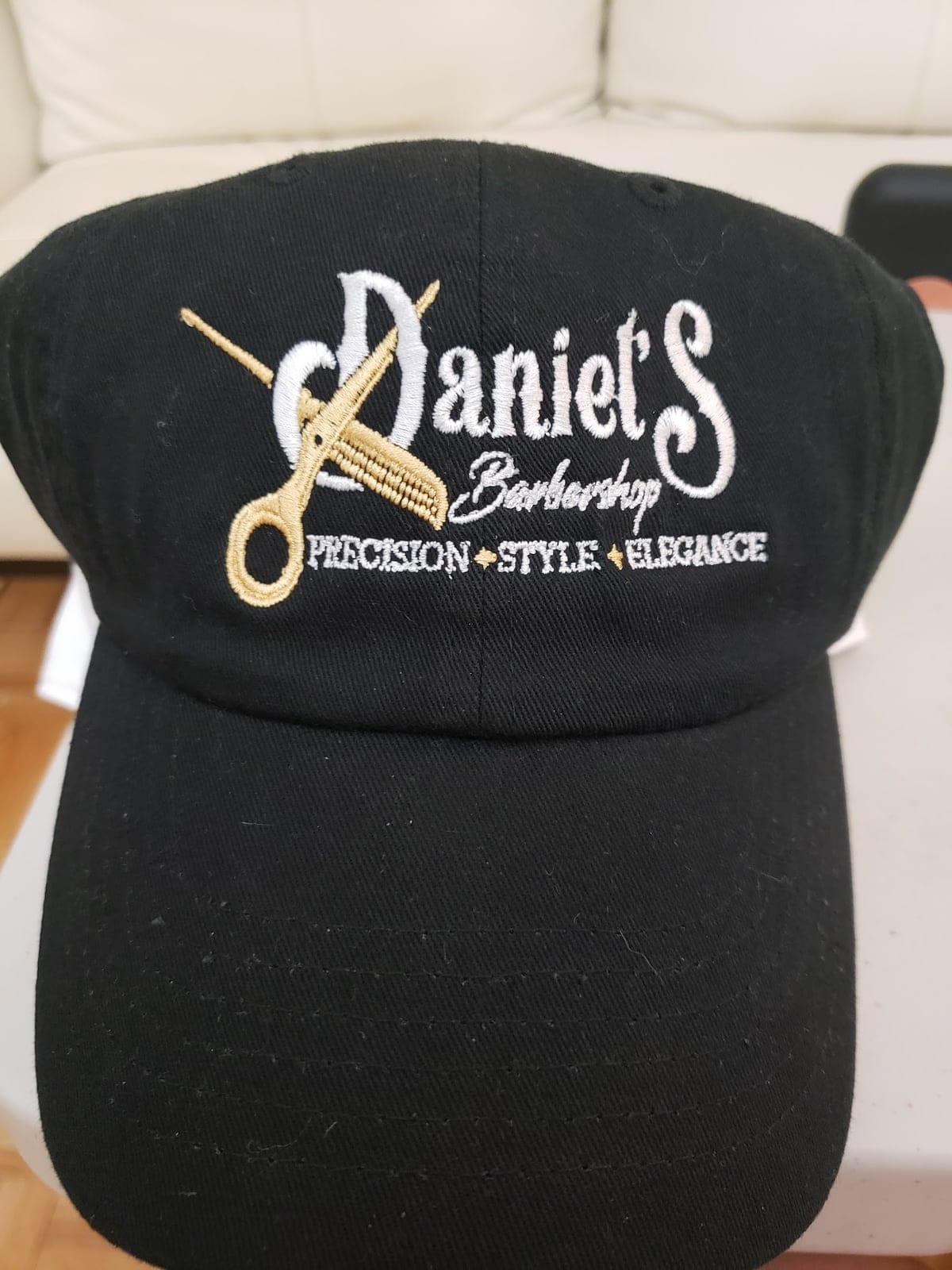 Black Daniel’s Barbershop cap with the gold scissors-and-comb logo