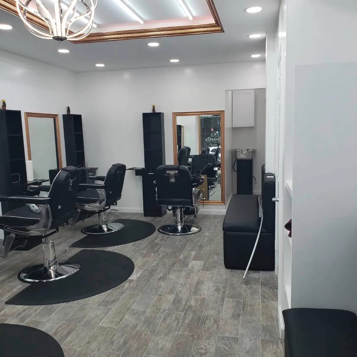 Black barber chairs on round mats under the chandelier and gold-trimmed ceiling