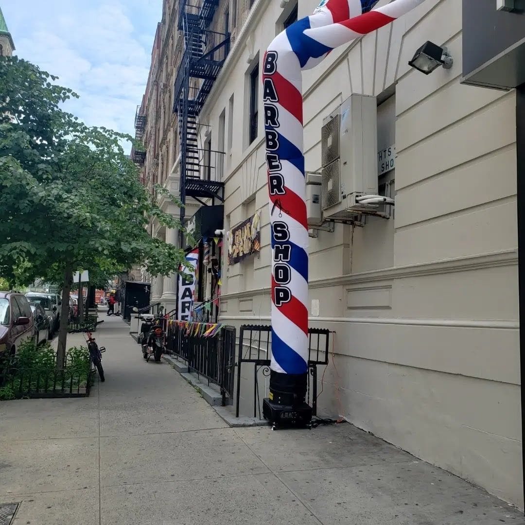 A striped barber pole banner on West 99th Street outside the shop