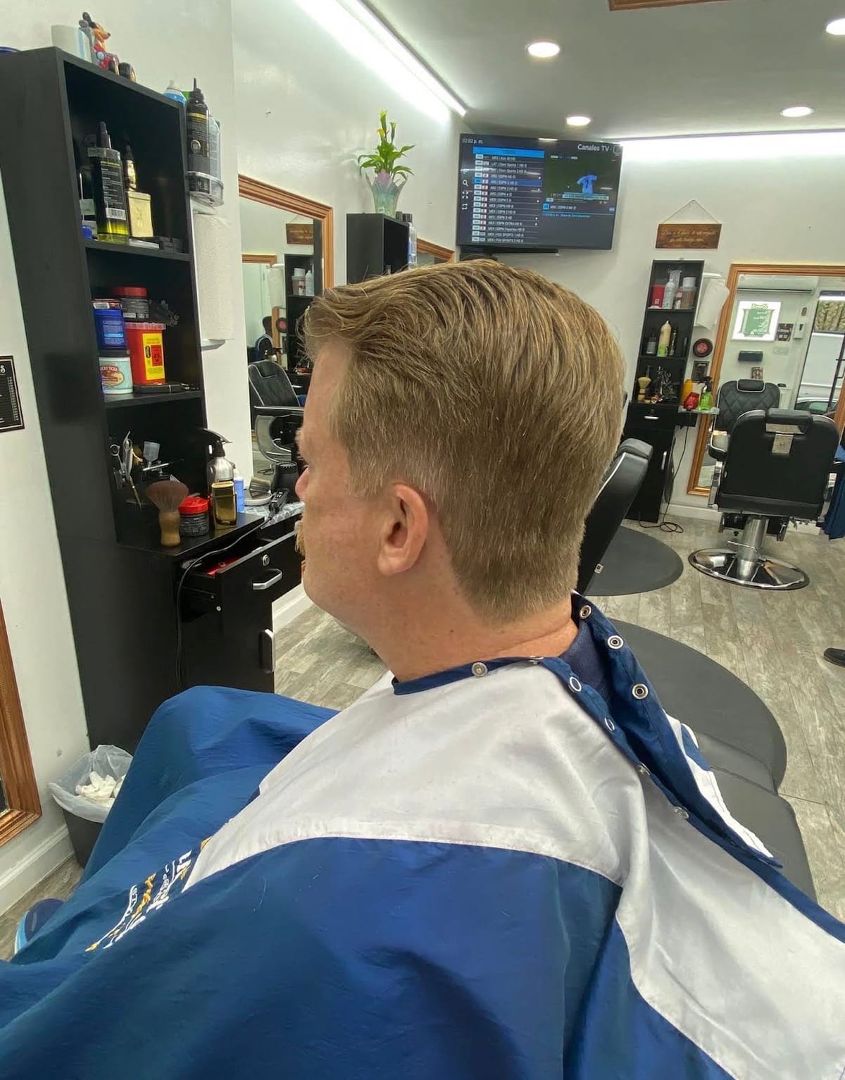 Back and side view of a tapered, side-swept cut in front of the black shelving and gold mirrors